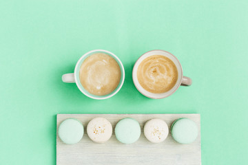 Fashion flat lay with two cup of coffee and tasty macaroons on trend color mint background with copy space. Sweet food and hot cappuccino in big mug. Morning concept. Top view.
