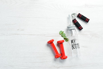 Fitness dumbbells, expander and water bottle. On a white wooden background. Flat lay.