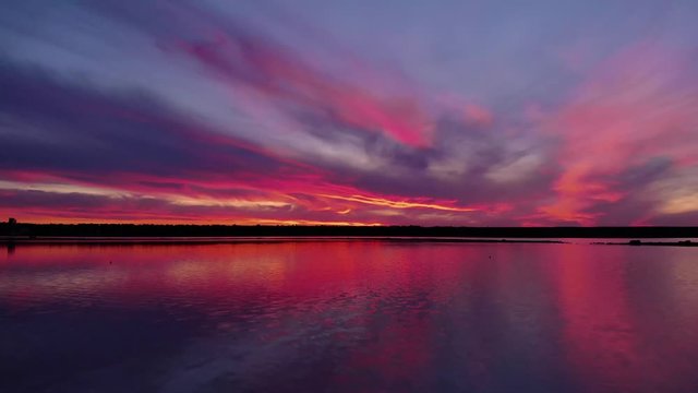 Aerial view of drone slide over water surface in twilight, golden hour sunset. Cinematic shot camera flies over calm firth surface reflecting majestic red and pink clouds