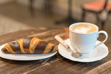 Fresh and tasty croissants with chocolate and cup of coffee on wooden background