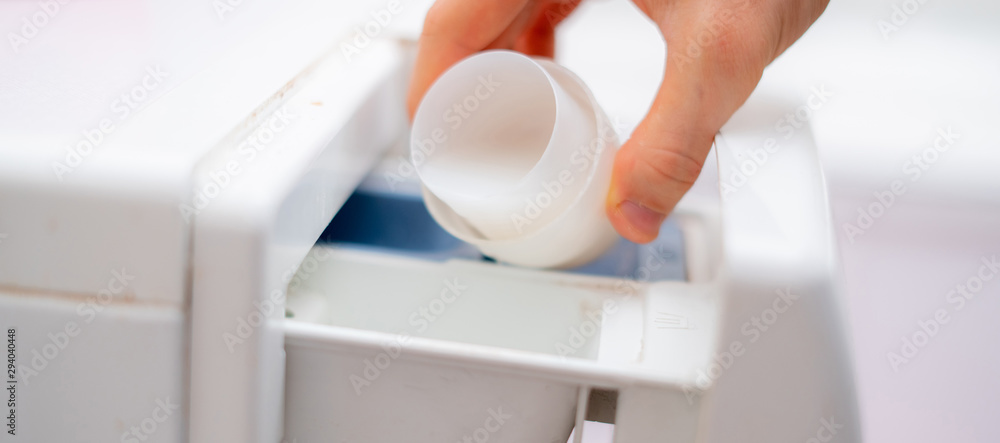 Wall mural pouring the washing conditioner in the washing machine to get clean clothes