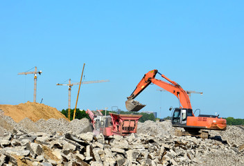 Obraz premium Heavy tracked excavator load stone, old asphalt or concrete waste into a mobile jaw crusher machine. Crushing and processing into gravel for recycling in concrete or cement production.