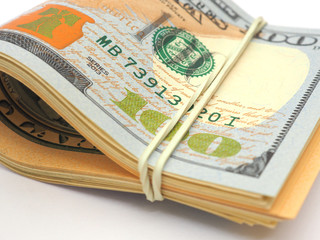 A rolled up bundle of dollars lies on a white paper background. Above is the hundred-dollar bill of the last sample. Denominations are connected by an elastic band. Close-up