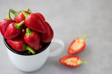 Red chili peppers in a white metal mug on a gray background.