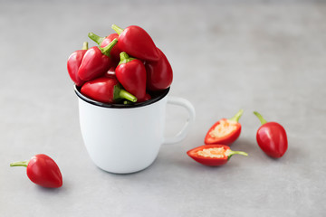 Red chili peppers in a white metal mug on a gray background.