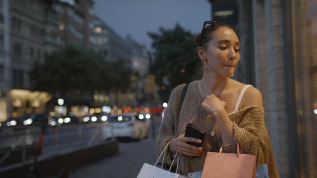 A young woman with multiple shopping bags looking through a shop window at goods