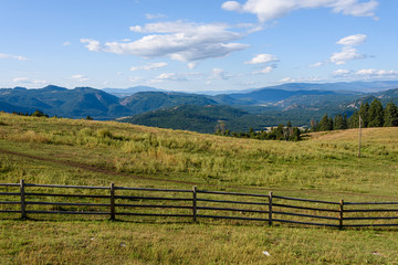 Fototapeta na wymiar Tranquil scene in early morning light of hilltop pasture with wood fence line and sky and mountains in background