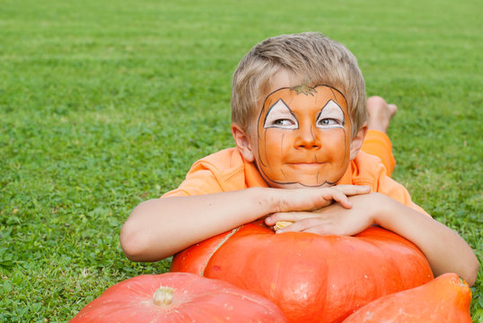 Cute, young boy dressed for Halloween lying on a pumpkin