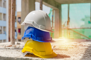 white, blue and yellow hard safety helmet for safety accident stack on floor at workplace in...