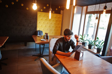Confident young indian man in black shirt sitting at cafe and read menu.
