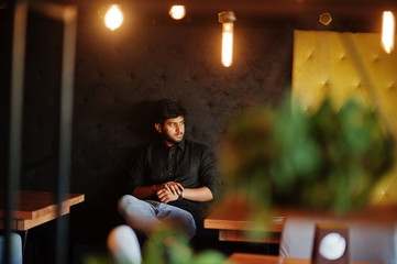 Confident young indian man in black shirt sitting at cafe.