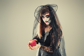 woman in a carnival costume of a witch or a dead bride holding an apple in her hands, gothic woman...