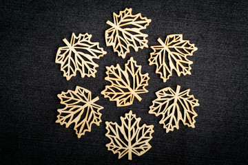 Seven delicate light brown wooden leaves on dark grey textile material background, displayed as a flower, top view with space for text on the right side, flat lay with laser cut wooden objects