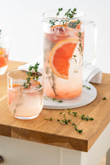 Lemonade with grapefruit and thyme in a glass jug on light background.