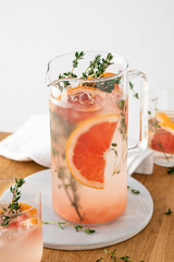 Lemonade with grapefruit and thyme in a glass jug on light background.