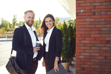 Businessman and business woman standing smiling outdoors.