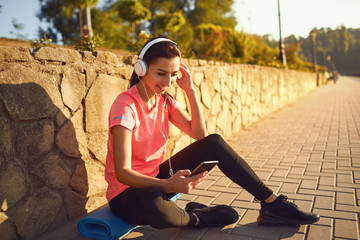 Fototapeta premium A sports girl in headphones is resting listening to music after training.