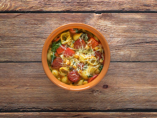 spicy chorizo sausage stew with vegetables and greens on wooden table, top view