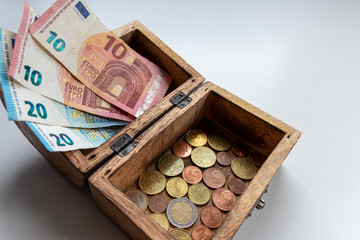 Euro-Scheinen und Euro-Münzen in einer offenen Schatztruhe aus Holz zeigen Reichtum,...