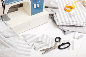 process of sewing of bed linen on sewing machine. Sewing kit. Grey fabric, scissors, threads, measuring tape and sewing machine on white wooden background