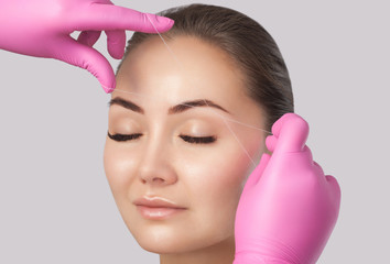 The make-up artist plucks eyebrows with a thread close-up. Face care, beauty treatments in the...