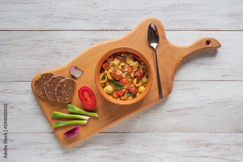 Wall mural Spicy chorizo sausage stew with vegetables and greens on wooden table, top view. 