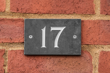 Dark grey house number 17 sign against a brick wall.