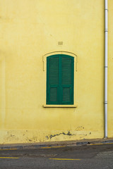 Fototapeta na wymiar Little green window shutters on a pastel yellow wall shot straight on.