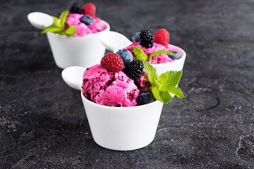 Homemade berry sorbet in white cups and fresh berries on a black background.