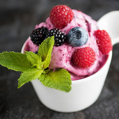 Homemade berry sorbet in white cup and fresh berries on a black background.