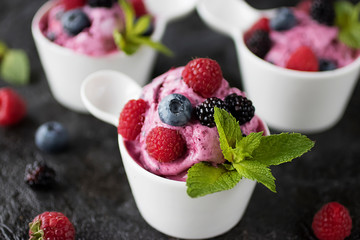 Homemade berry sorbet in white cups and fresh berries on a black background.