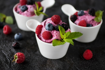 Homemade berry sorbet in white cups and fresh berries on a black background.