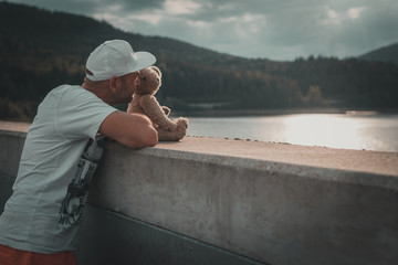 Mann mit Teddybär blickt über die Mauer auf den See