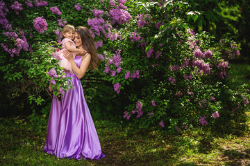 Authentic mother is holding on hands her little daughter. They standing among flowering trees. Copy space
