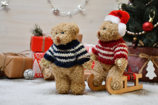 A Teddy Bear takes another one for a sledge drive on a background of a Christmas tree & boxes with Christmas presents