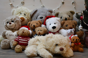 Twelve various Teddy Bears & a Christmas tree nearby on a background of a white wooden surface