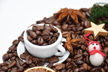A small cup, coffee beans nearby, a gold star, a snowman & a green heart, a star-anise & a dried orange slice nearby