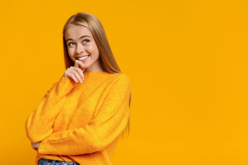 Pensive teen girl looking upwards on orange studio background