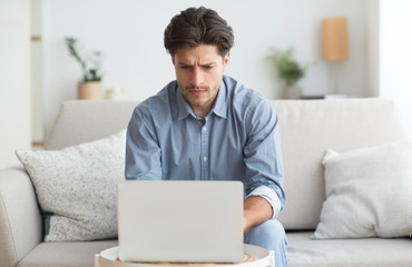 Man Working At Laptop Sitting On Couch At Home