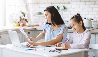 Mother working from home while daughter doing homework in kitchen
