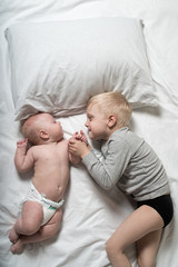 Baby and smiling older brother are lying on the bed. They play, communicate and interact. Top view