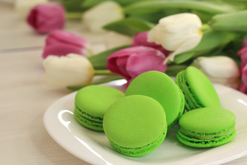 Tasty macarons and tulips on table, close up