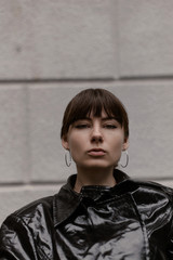 Stylish girl in a black cloak and dress on a background of a gray wall