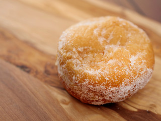 One doughnut with sugar glaze on a wooden background. Warm tones. Selective focus.