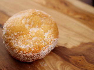 One doughnut with sugar glaze on a wooden background. Warm tones. Selective focus.