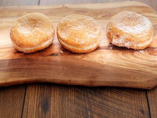 Three doughnuts with sugar glaze on a wooden board and table.