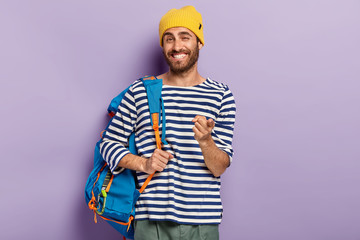 Photo of glad smiling man traveler points at you with index finger, carries rucksack with necessary...
