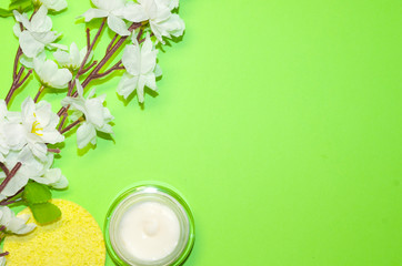 Beautiful composition with cosmetics on light green background, flat lay with skin cream and wthite flowers, spring background with a copy space for an your text, clean beauty concept, top view