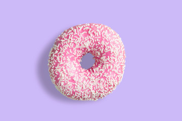 One pink donut with white sprinkles on a purple background. Fresh donut poured with pink glaze.