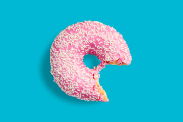 One bitten pink donut with white sprinkles on a blue background. Fresh donut poured with pink glaze.